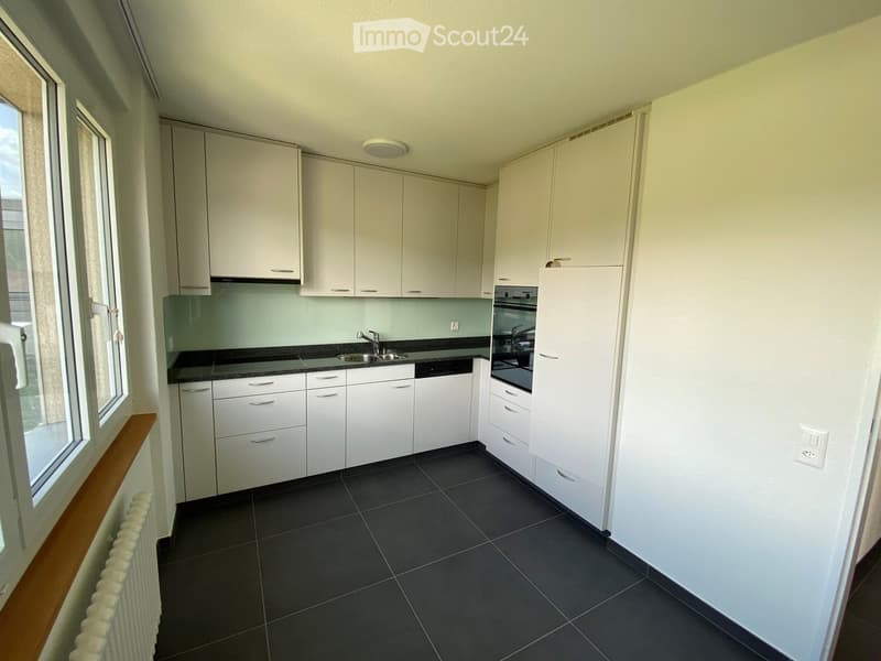 Modern kitchen with white cabinets, dark tiled floor, and stainless steel appliances including a sink and oven.