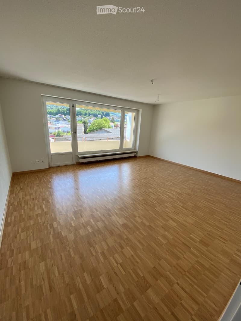 Empty room with wooden flooring, large windows, and a sliding glass door leading to a balcony.