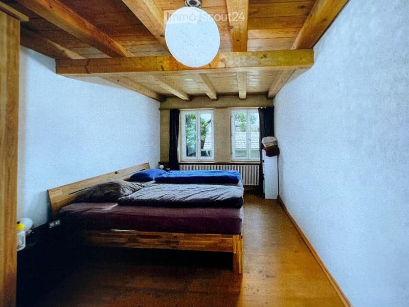 Cozy bedroom with wooden bed, pillows, radiator, and exposed wooden ceiling beams.