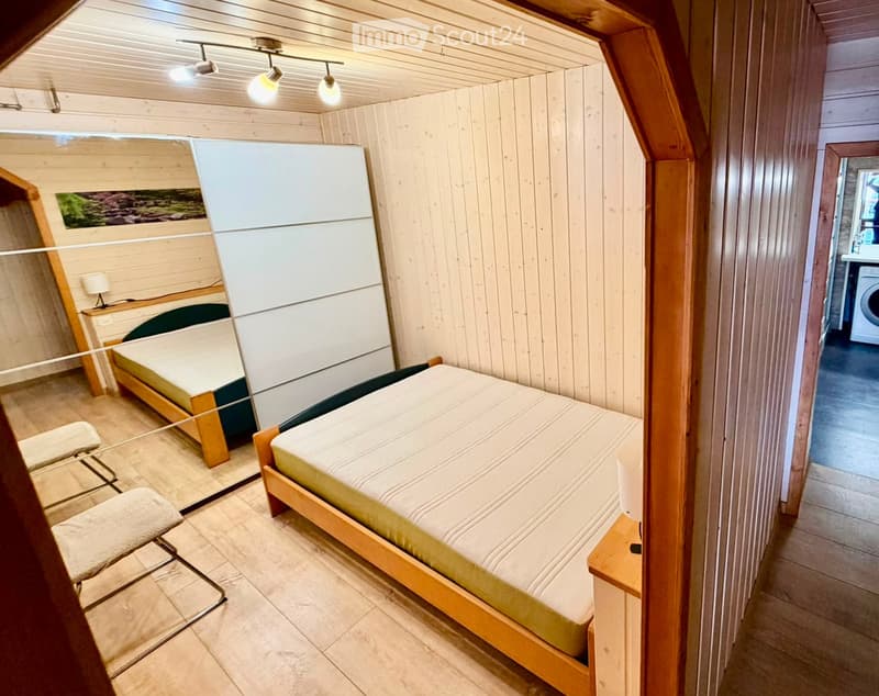 Cozy wooden bedroom with two single beds, a chair, a mirror, and a nightstand with a lamp.