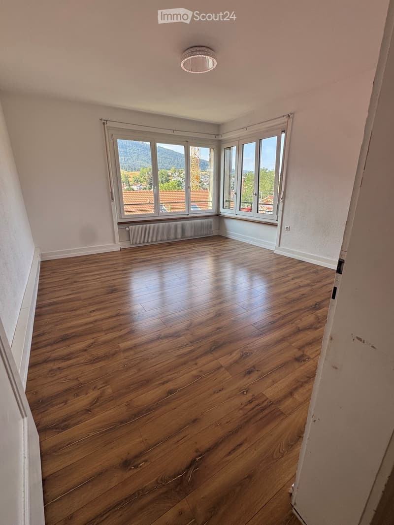 Empty room with wooden flooring, large windows, and a radiator under the windows.
