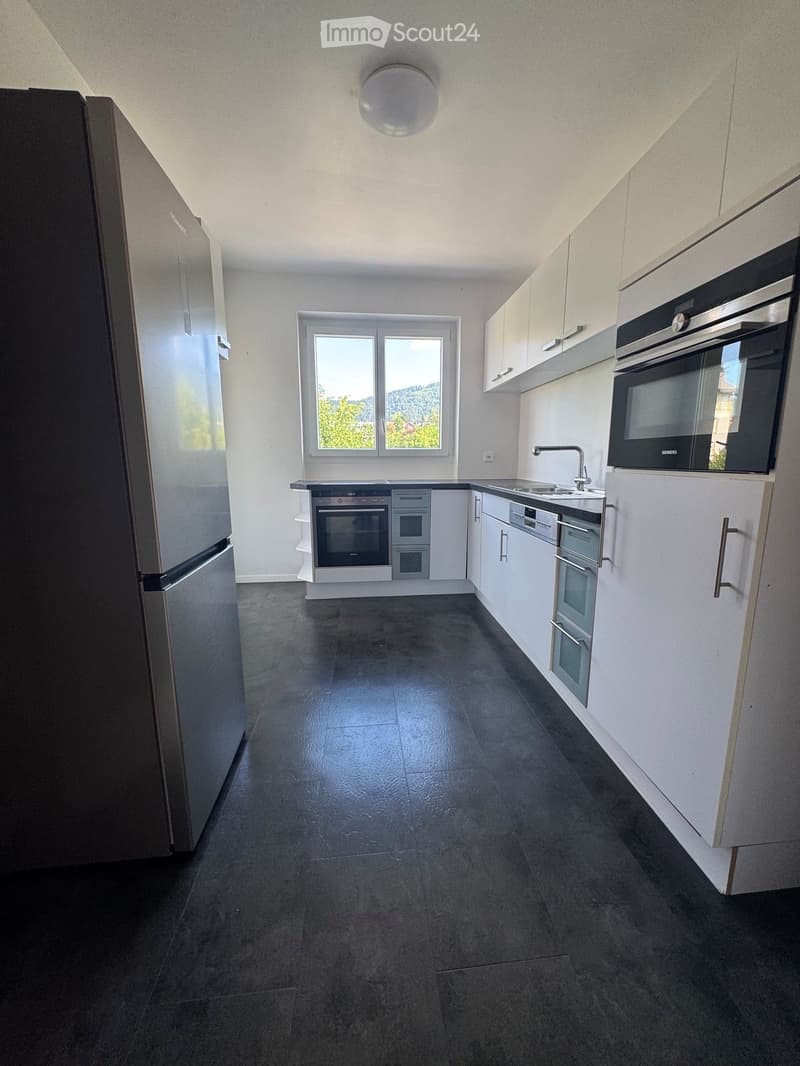 Modern kitchen with white cabinets, stainless steel appliances, dark tiled floor, and a window offering a view of greenery.