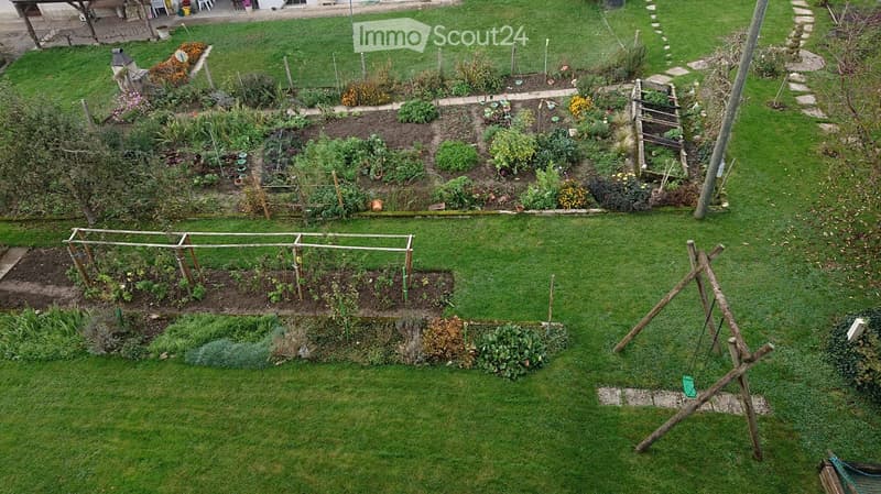 Well-maintained garden with various plants, raised beds, and a swing set.