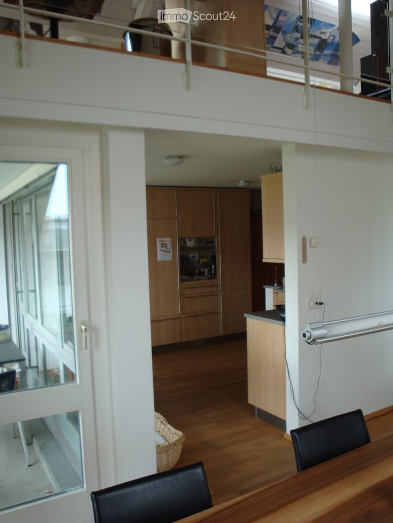 Open-plan living and dining area with wooden flooring, modern kitchen cabinets, and a dining table with chairs.