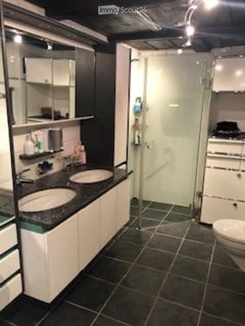 Modern bathroom with double sink, large mirror, white cabinets, and a glass-enclosed shower area.