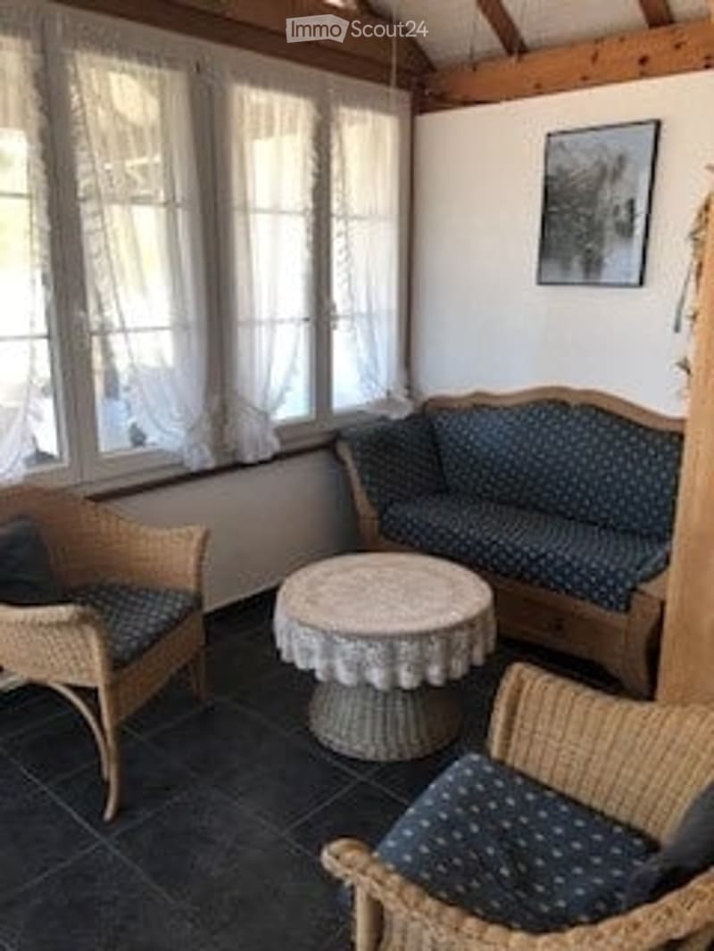Cozy living room with large windows, a patterned sofa, a round coffee table, and wicker chairs.