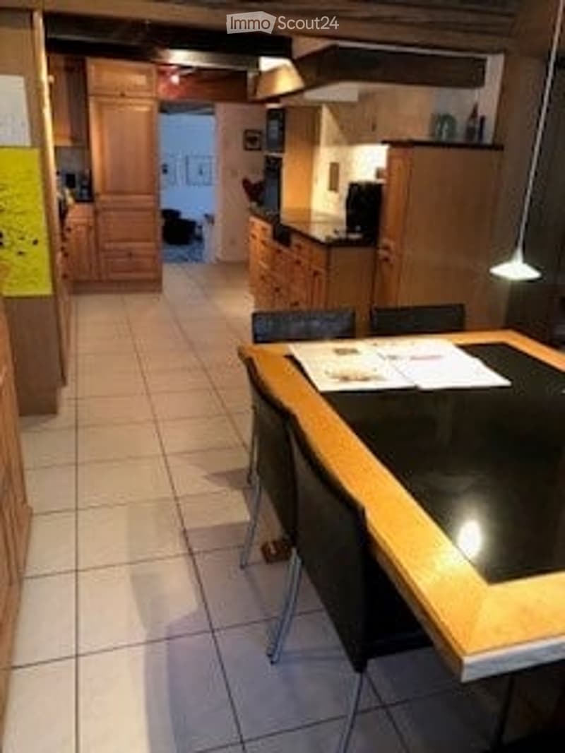 Bright, open-plan kitchen and dining area with light wooden cabinets, a black dining table with four chairs, and a tiled floor.