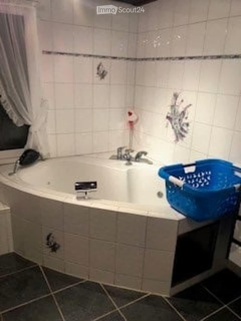 Bathroom with a large, curved bathtub, white tiled walls, a shower basket on the edge, and a curtain on the left side.