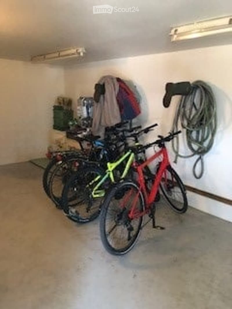 Garage with three bicycles, a jacket, and a coiled rope on the wall.