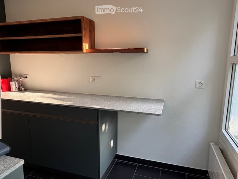 Modern kitchen with dark grey cabinets, a light grey countertop, and a wooden shelf above.