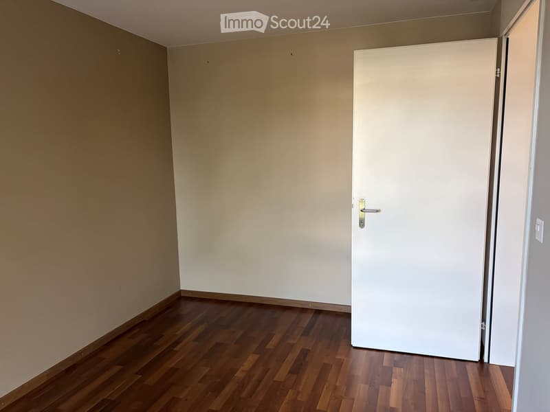 Empty room with wooden flooring and white walls, featuring a closed white door.