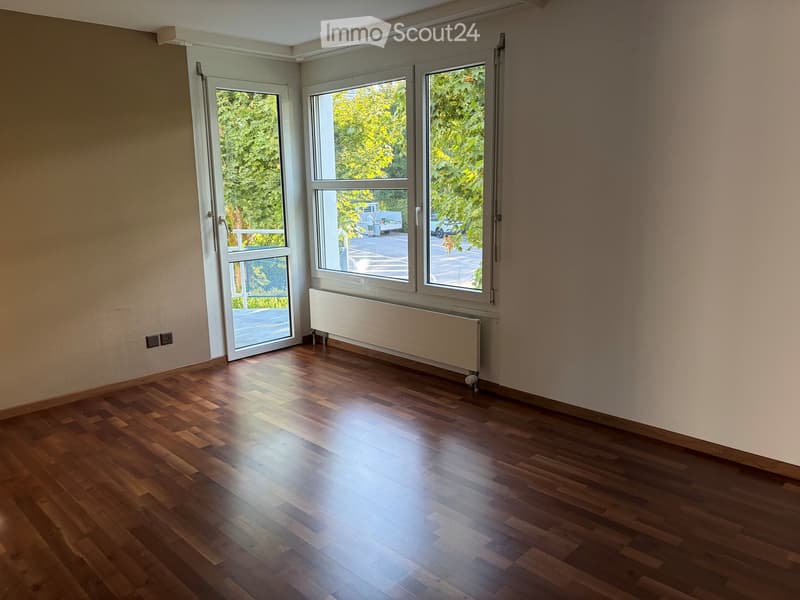 Empty room with wooden flooring, large windows, and a radiator. No furniture or equipment present.