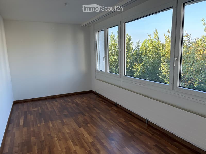 Empty room with wooden flooring, white walls, large windows, and radiator under the windows.