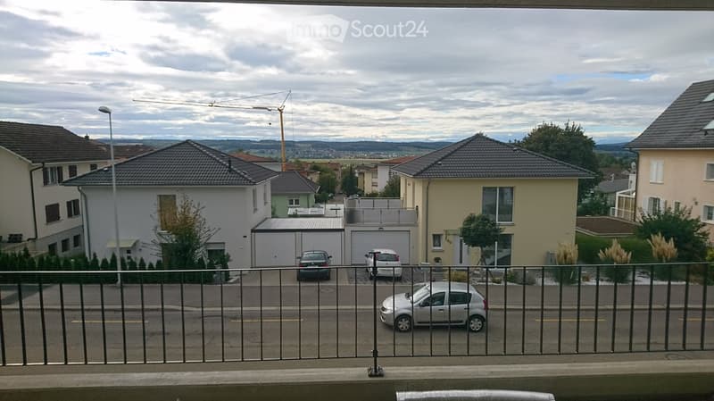 Balcony overlooking a residential street with houses, parked cars, and a distant view of mountains and a construction crane.