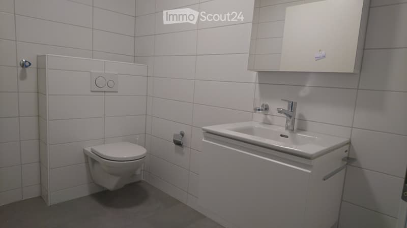 Modern bathroom with white tiles, a toilet, a sink with a modern faucet, and a white cabinet above the sink.