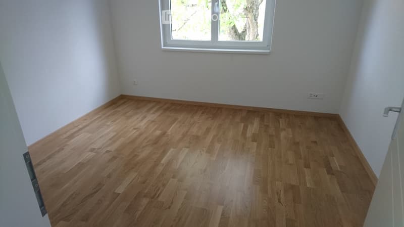 Empty room with light wooden flooring and white walls, featuring a single window and electrical outlets.