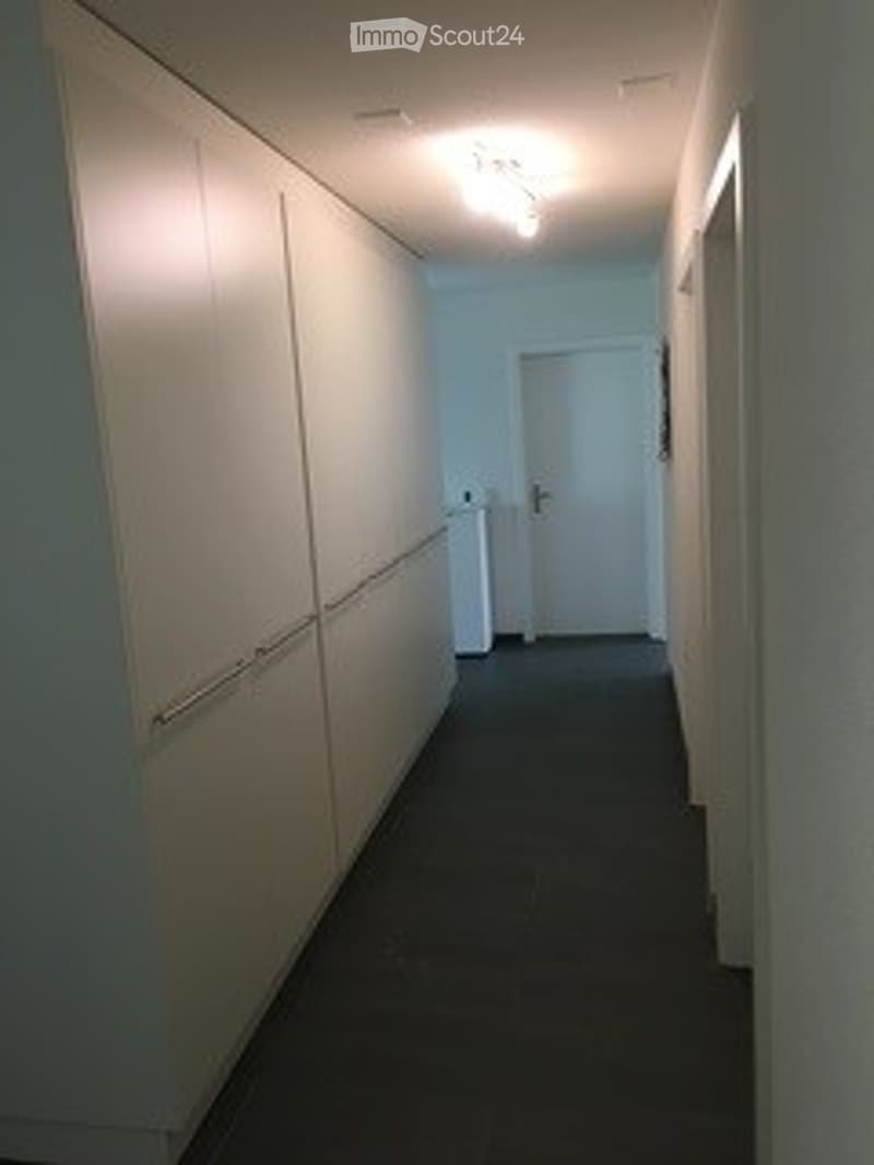Empty hallway with white walls, dark carpeted floor, and a closed white door at the end.