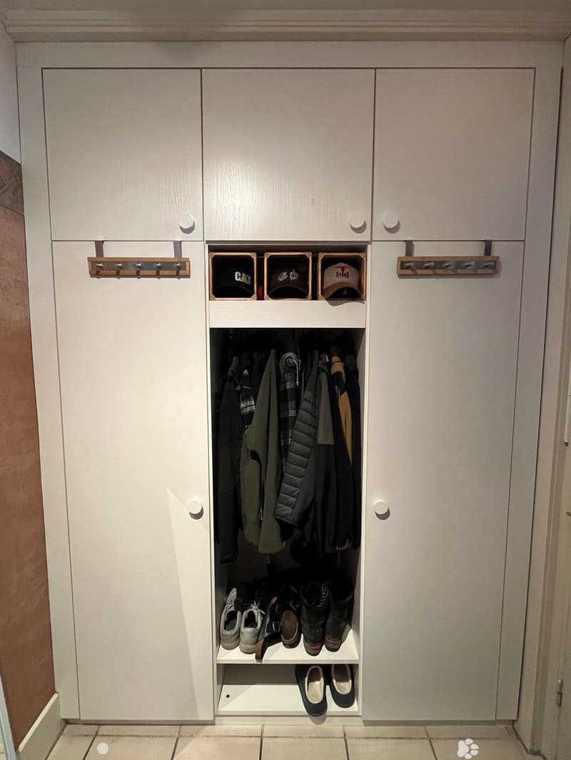 A modern hallway closet with white cabinetry, multiple storage compartments, and organized clothing and shoes inside.
