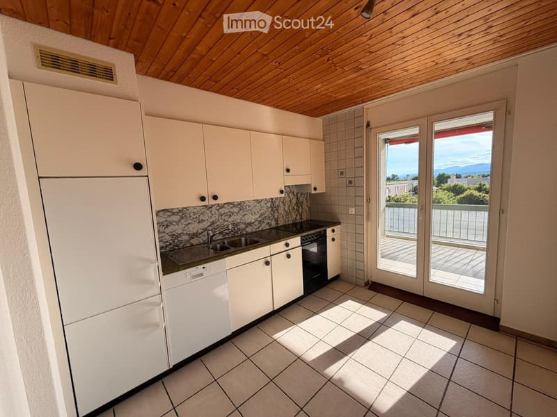 Modern kitchen with white cabinets, stainless steel appliances, and a marble backsplash, leading to a balcony with a scenic view.