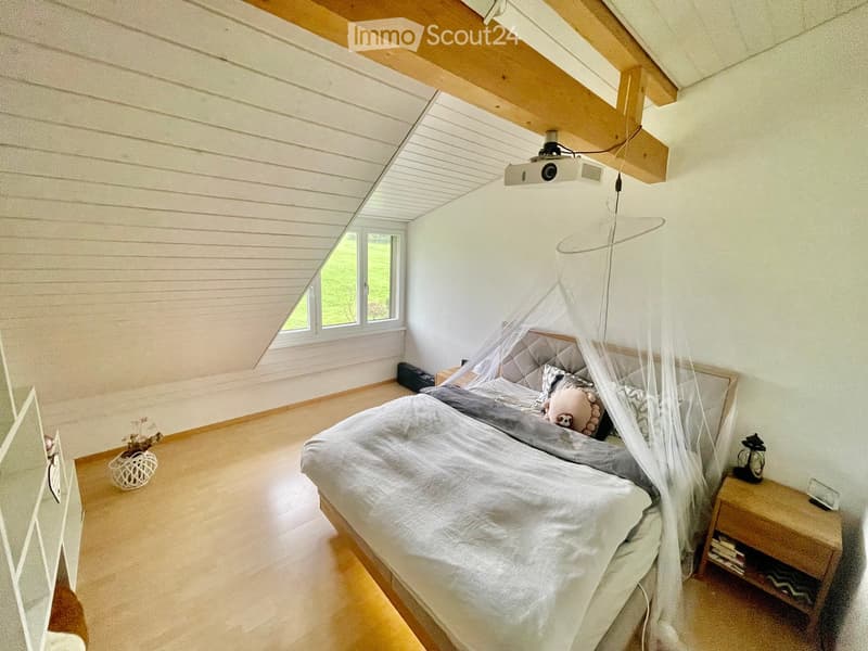 Cozy attic bedroom with wooden slat ceiling, skylight windows, a large bed with a canopy, nightstands, and a projector mounted on the ceiling.