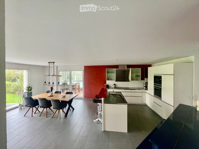Modern kitchen with white cabinets, stainless steel appliances, a dining area with a wooden table and chairs, and pendant lighting.