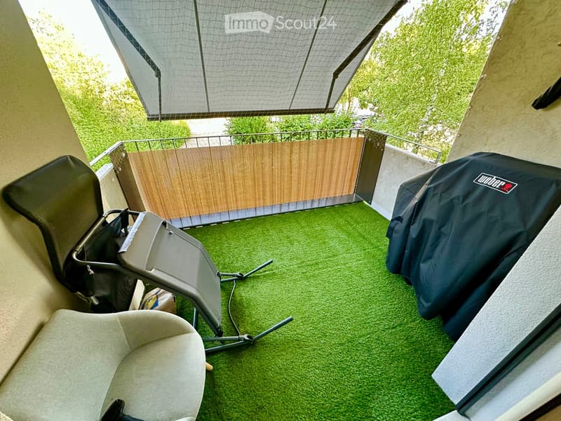 Balcony with artificial grass flooring, covered seating area, grill, and outdoor furniture.