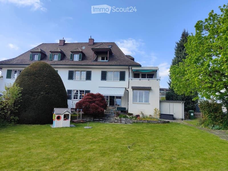 Two-story house with a well-maintained garden, featuring a large lawn, a playhouse, and a swing set.