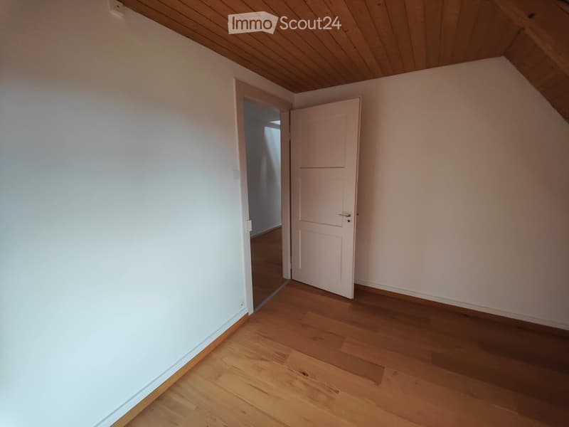 Empty room with wooden flooring, white walls, and a partially open door leading to another space.