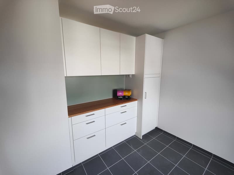 An empty room with white cabinets, a wooden countertop, and dark tiled flooring.