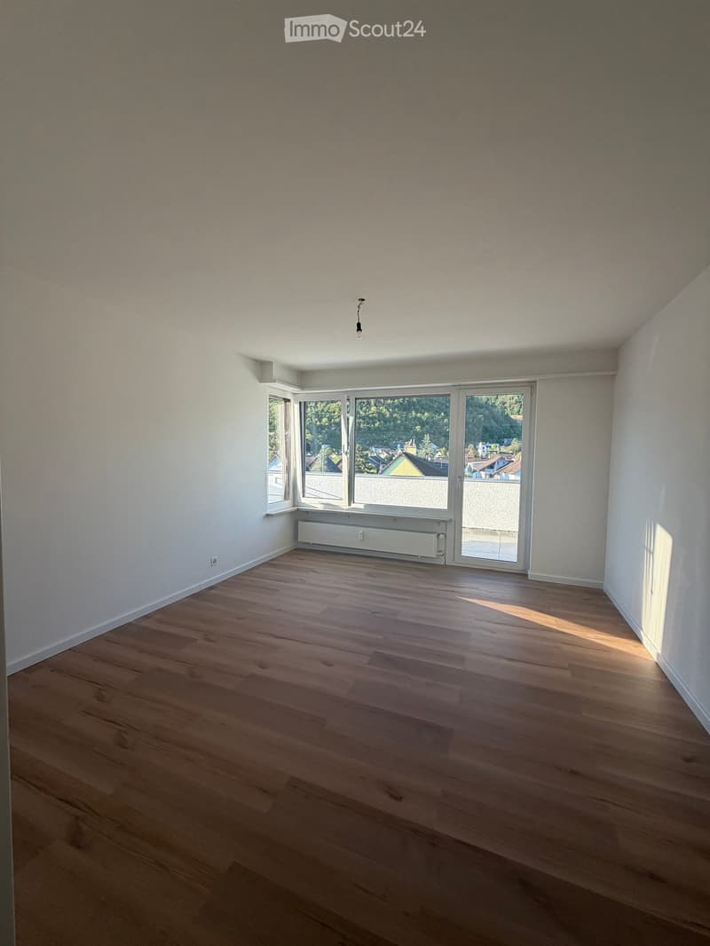 Empty room with wooden flooring, white walls, large windows, and a radiator. No furniture or equipment present.