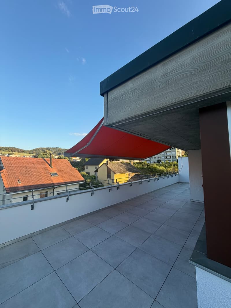 Balcony with tiled floor, white walls, metal railing, and a red retractable awning extending from the roof.