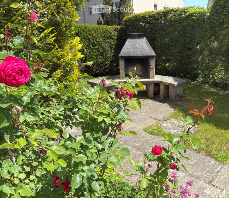 Garden with roses, a stone bench, and a small stone barbecue in the background.