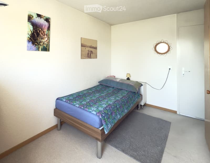 Cozy bedroom with a single bed, nightstand, lamp, and two picture frames on the wall.