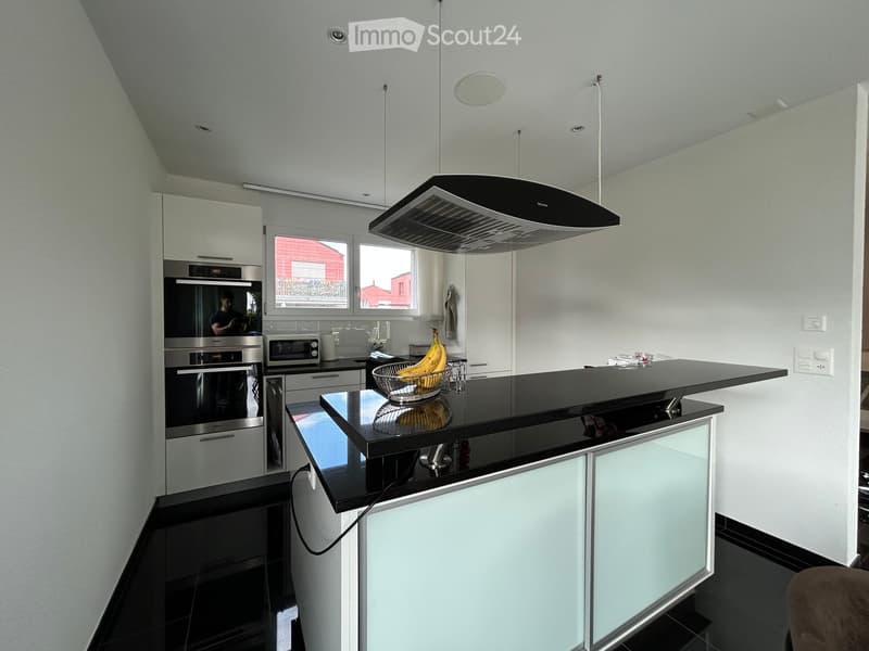 Modern kitchen with white cabinets, black countertops, stainless steel appliances, and a central island with a fruit bowl.