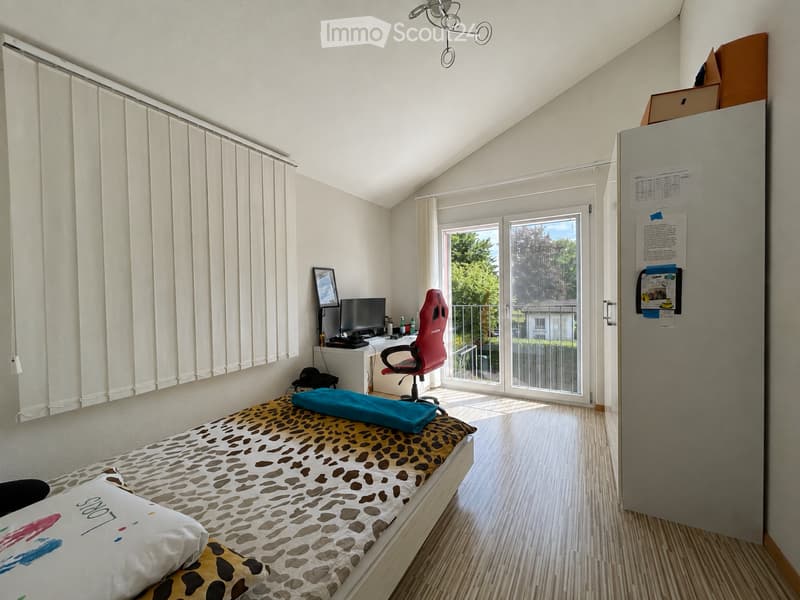 Bedroom with a single bed, desk, chair, and computer. Features a large window with blinds and a sliding glass door leading to a balcony.