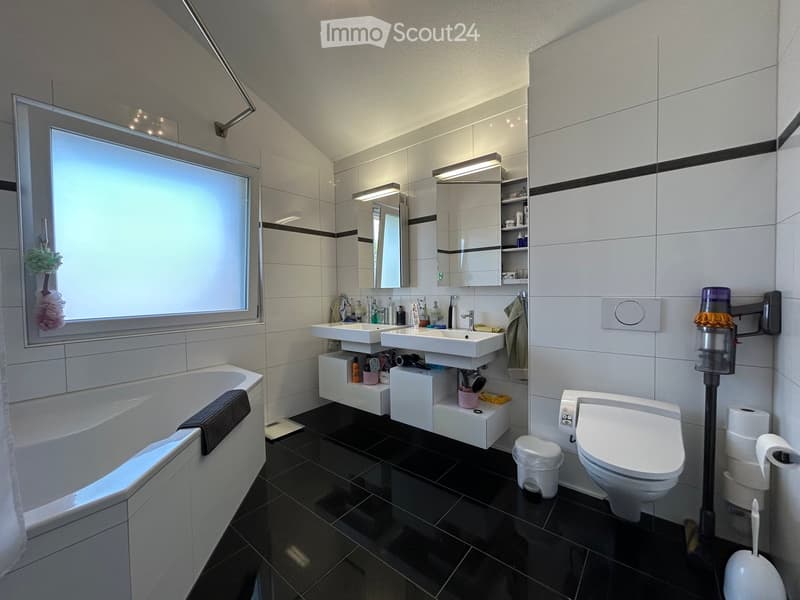 Modern bathroom with white tiles, black floor, double sink, bathtub, toilet, and large window.