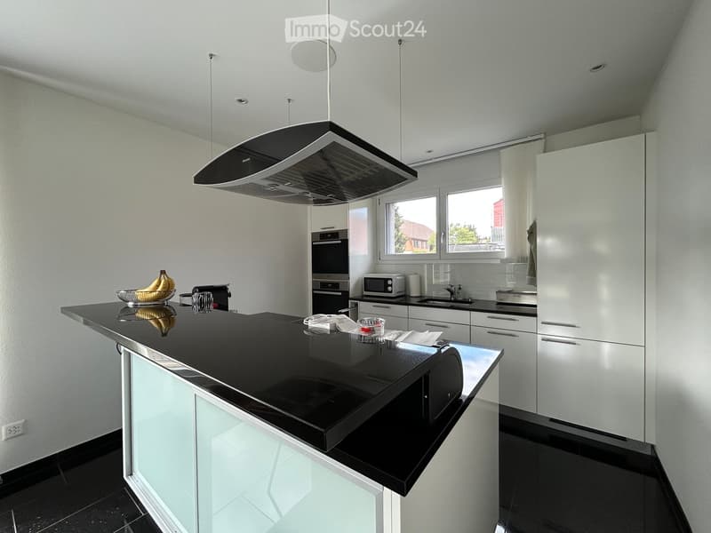 Modern kitchen with black countertops, white cabinets, stainless steel appliances, and a central island.