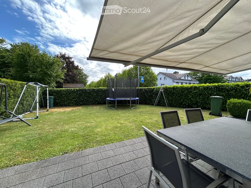 Backyard with a trampoline, swing set, patio furniture, and covered seating area.