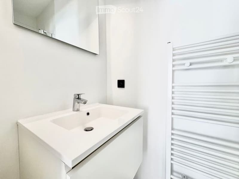 Modern bathroom with a white sink, chrome faucet, large mirror, and a white radiator.