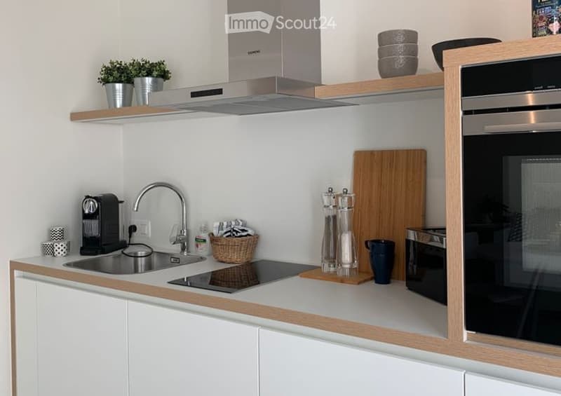 Modern kitchen with white cabinets, wooden accents, stainless steel appliances, and various kitchen items on the counter.