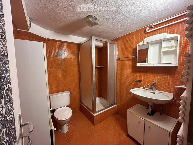 Bathroom with orange tiled walls and floor, featuring a toilet, sink with mirror, and a glass-enclosed shower. A towel rack is visible on the right side.