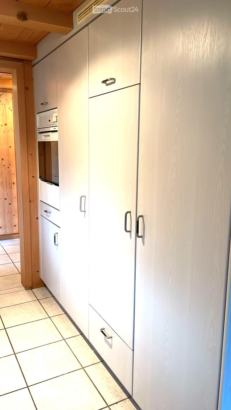 Modern kitchen with white cabinets, stainless steel handles, and tiled flooring. The cabinets are tall and have multiple drawers and doors.