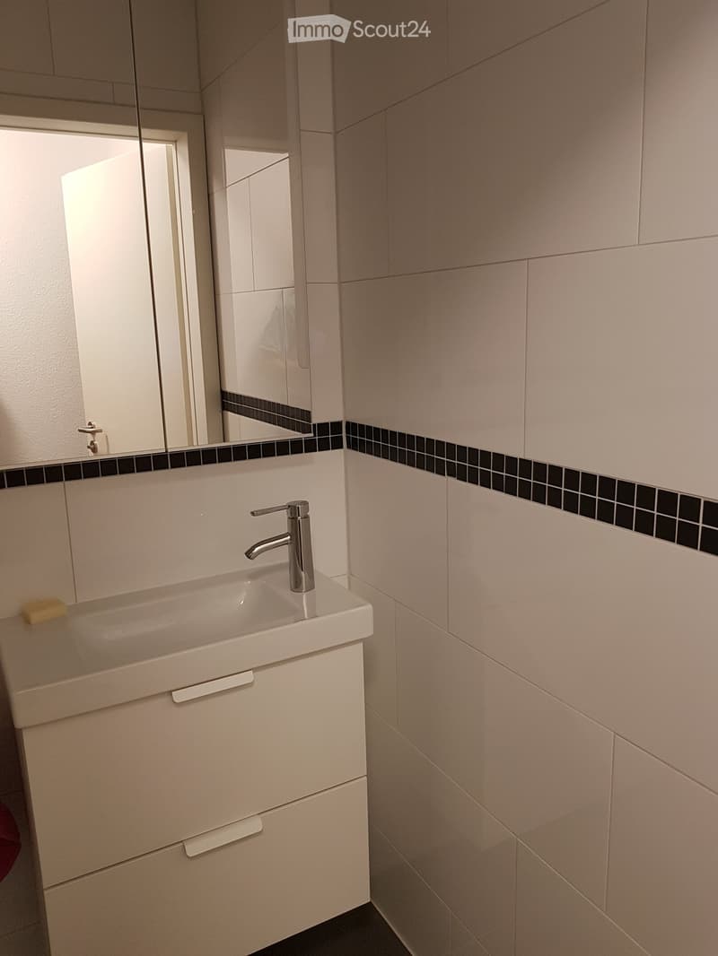Bathroom featuring a white sink with a silver faucet, white tiled walls, and a mirror mounted on the wall. Below the sink is a white cabinet with two drawers.
