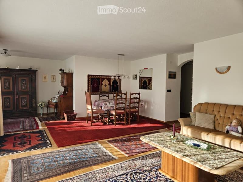 large living room, dining area, wooden dining table, wooden chairs, carpeted floor, wooden cabinet, couch, coffee table, wall art, mirror, ceiling lamp