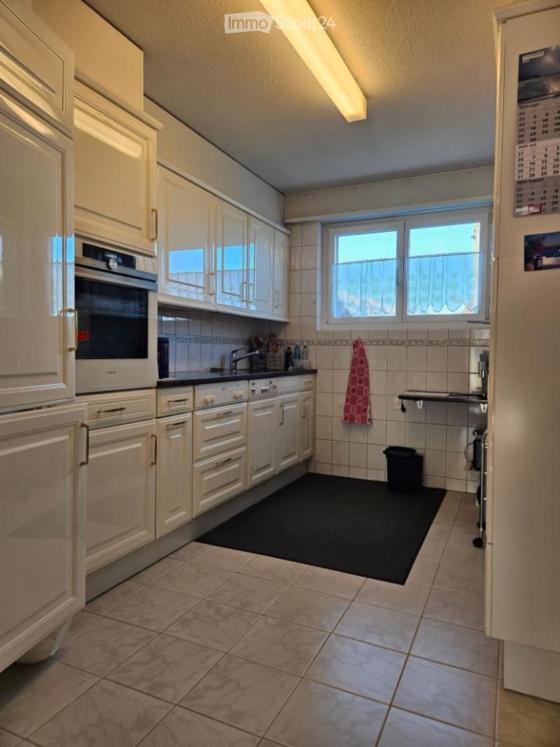 modern kitchen with white cabinets, tiled floor, black rug, built-in oven, dishwasher, washing machine, sink, window with curtains