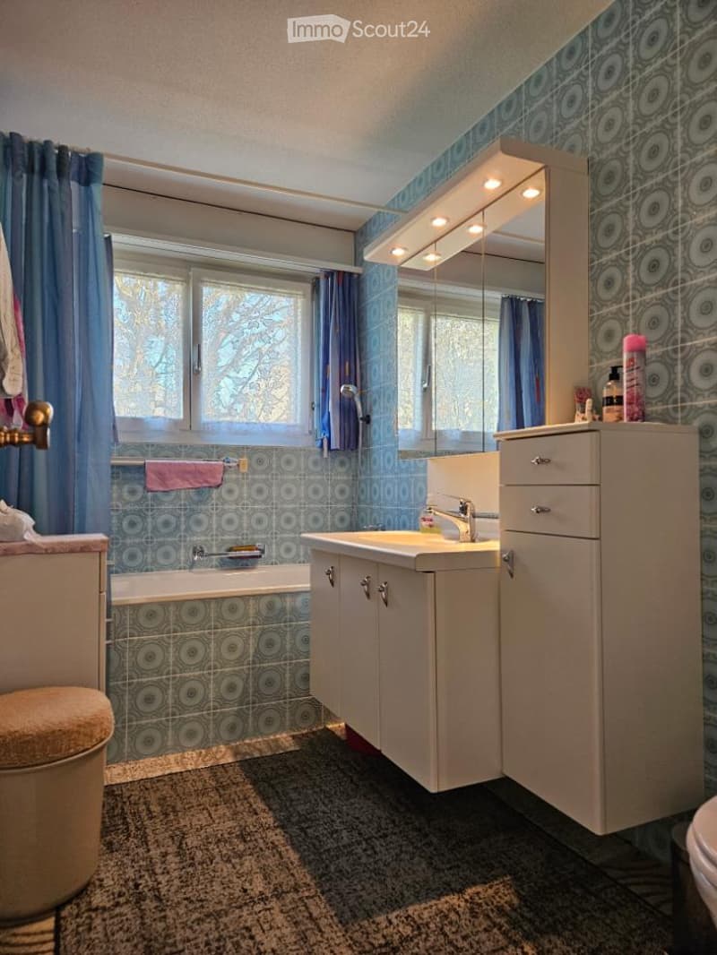 Bathroom with bathtub, sink, mirror, and tiled walls and floor.