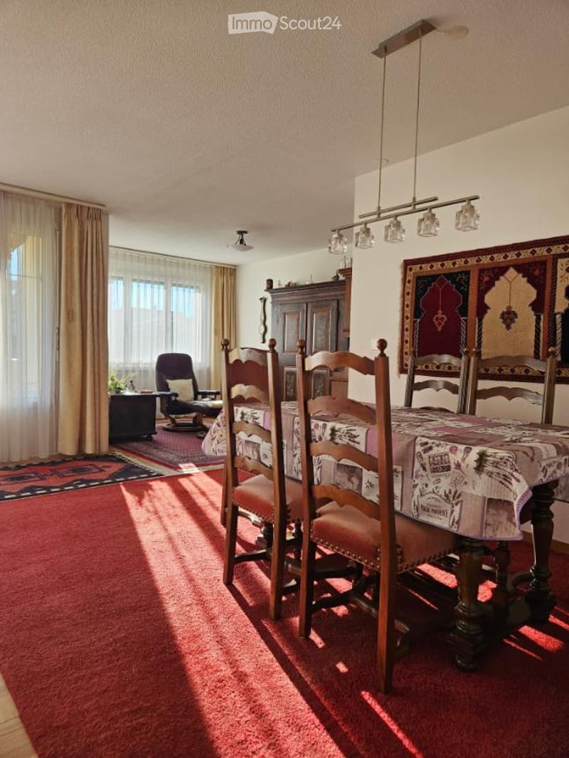 Dining room with wooden table and chairs, red carpet, chandelier, rug, cabinet, windows with curtains, wall art