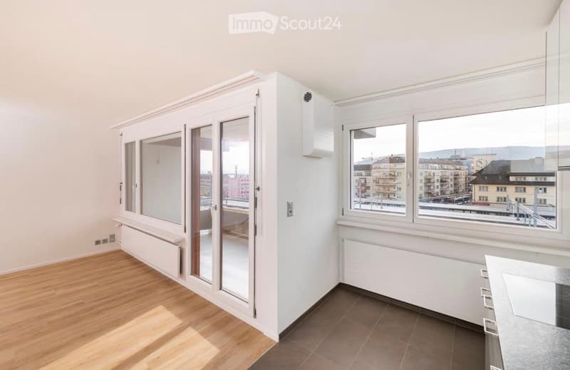 Empty room with wooden flooring, large windows offering a cityscape view, and white walls.