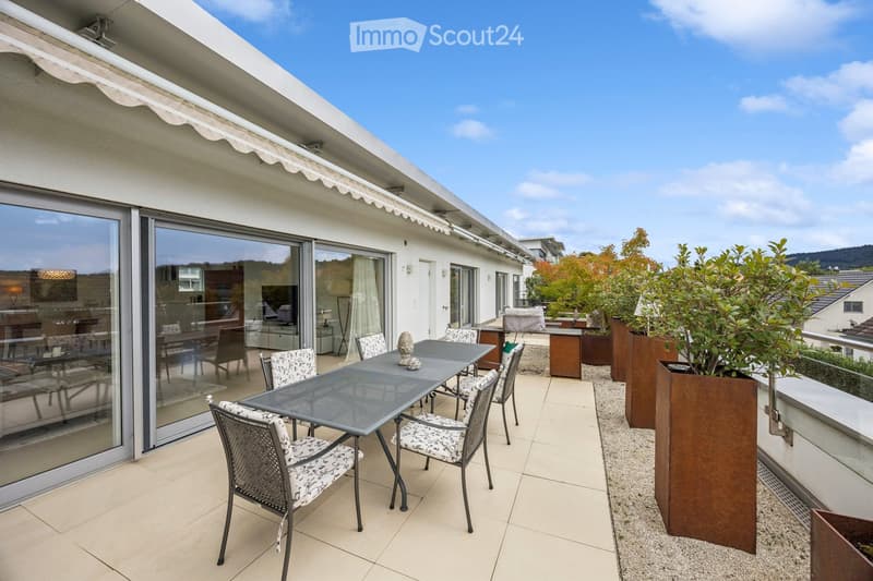 Balcony with a glass table and chairs, large sliding glass doors leading to the interior, potted plants, and a scenic view.
