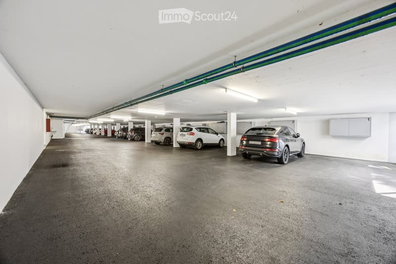 Underground parking area with several parked cars, white walls, and a concrete floor.
